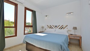 A bedroom with a bed, two bedside tables, a window, and a view of greenery outside. - Oliva - Central apartment with air conditioning 150 meters from the beach in Mallorca (Alcúdia)
