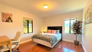 A bedroom with a bed, a desk, a chair, a window, and a potted plant.