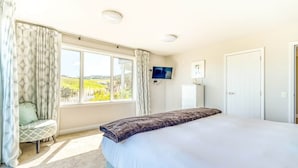 A bedroom with a large bed, a TV mounted on the wall, and a window with curtains.