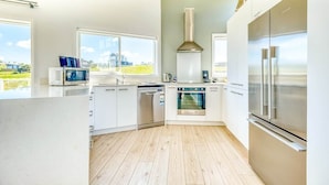 A modern kitchen with white cabinetry, stainless steel appliances, and large windows offering a view of the outdoors.