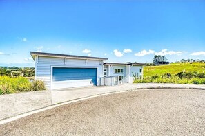 A single-story house with a garage, a driveway, and a grassy hill in the background.