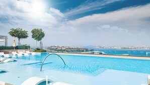 Una piscina con sillones de descanso y vista al mar.