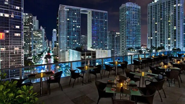 A rooftop restaurant with tables and chairs, a city view, and a pool. - The Club 4320 (Miami)