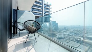 A balcony with two black wireframe chairs, a glass railing, and a cityscape view.