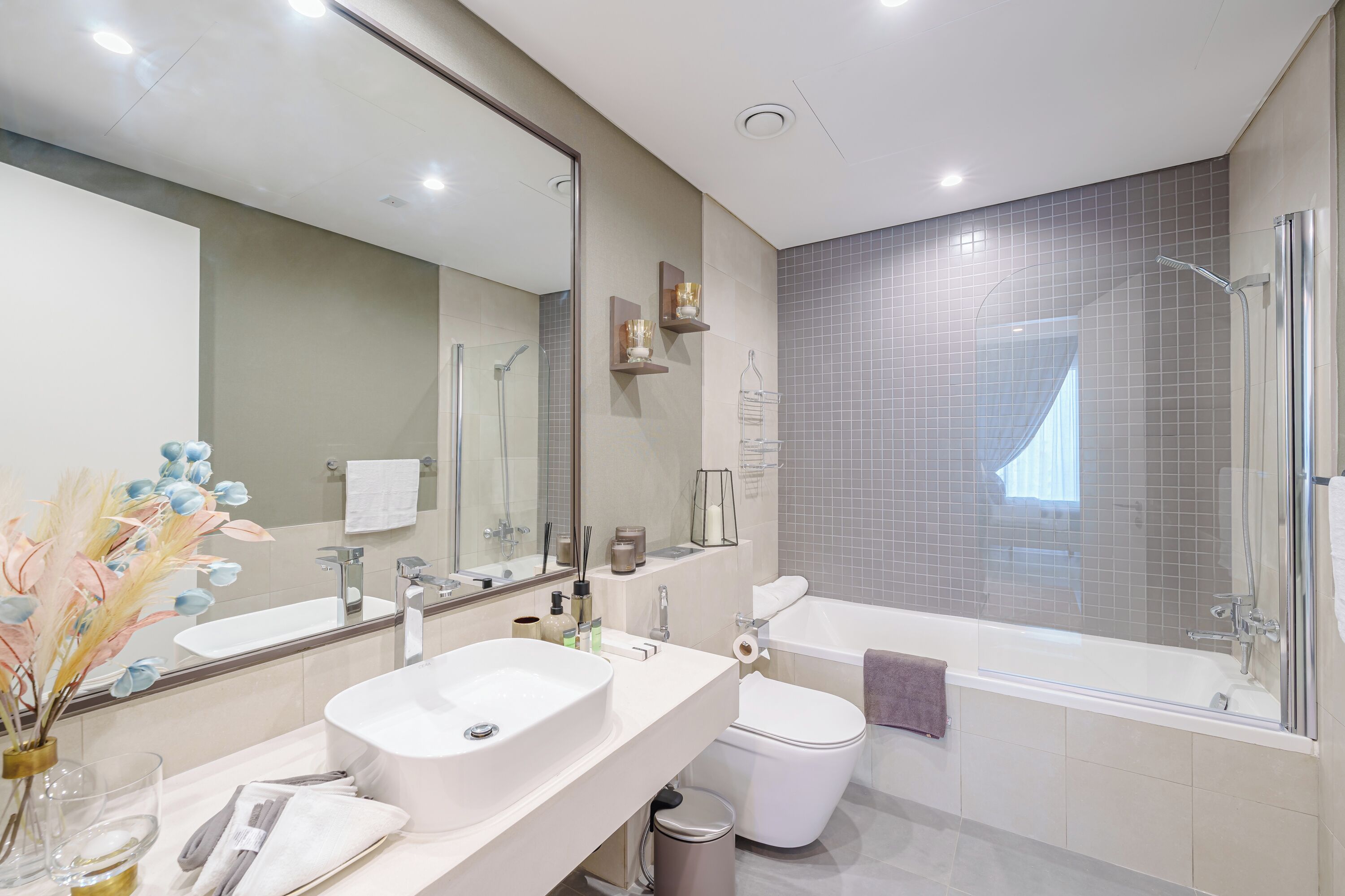 Een moderne badkamer met een grote spiegel, een wit wastafelmeubel, een toilet en een bad.