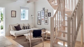 Uma sala de estar moderna com escada de madeira, sofá branco e quadros nas paredes.