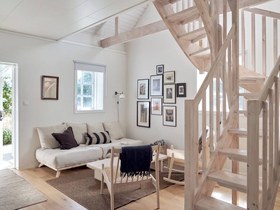 A modern living room with a wooden staircase, a white sofa, and framed pictures on the wall.