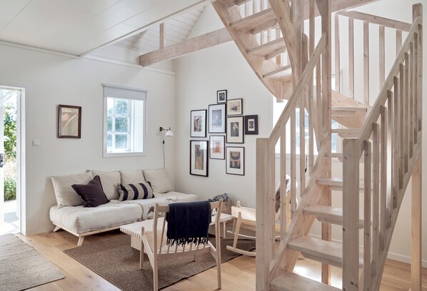 Un salon moderne avec un escalier en bois, un canapé blanc et des tableaux encadrés accrochés au mur.