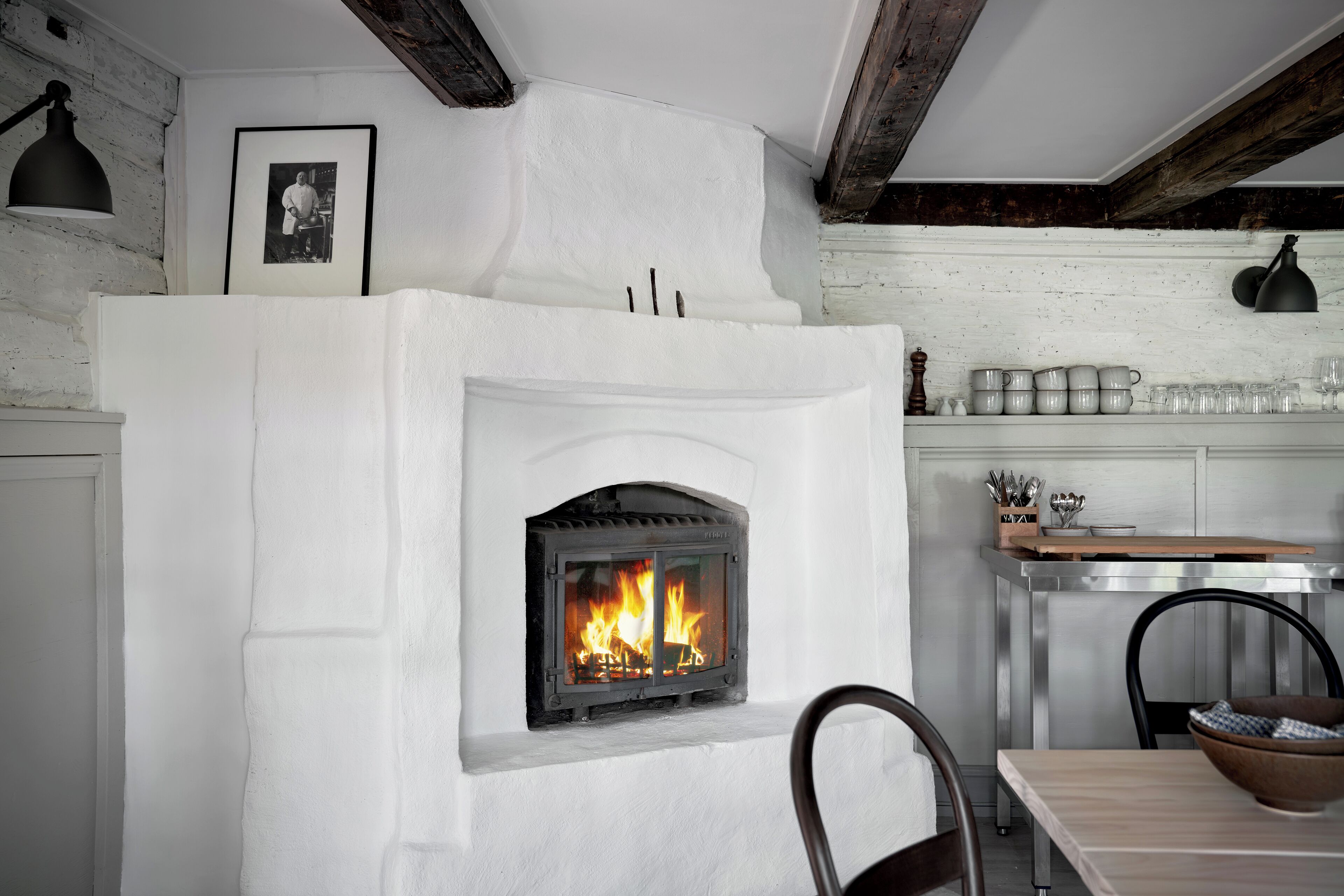 Une cheminée avec un feu apparent, un tableau encadré au mur et un coin repas avec des chaises et une table.