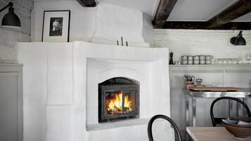 Une cheminée avec un feu apparent, un tableau encadré au mur et un coin repas avec des chaises et une table.