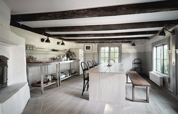Een ruime keuken met een groot eiland, houten balken in het plafond en uitzicht op de omgeving door grote ramen.
