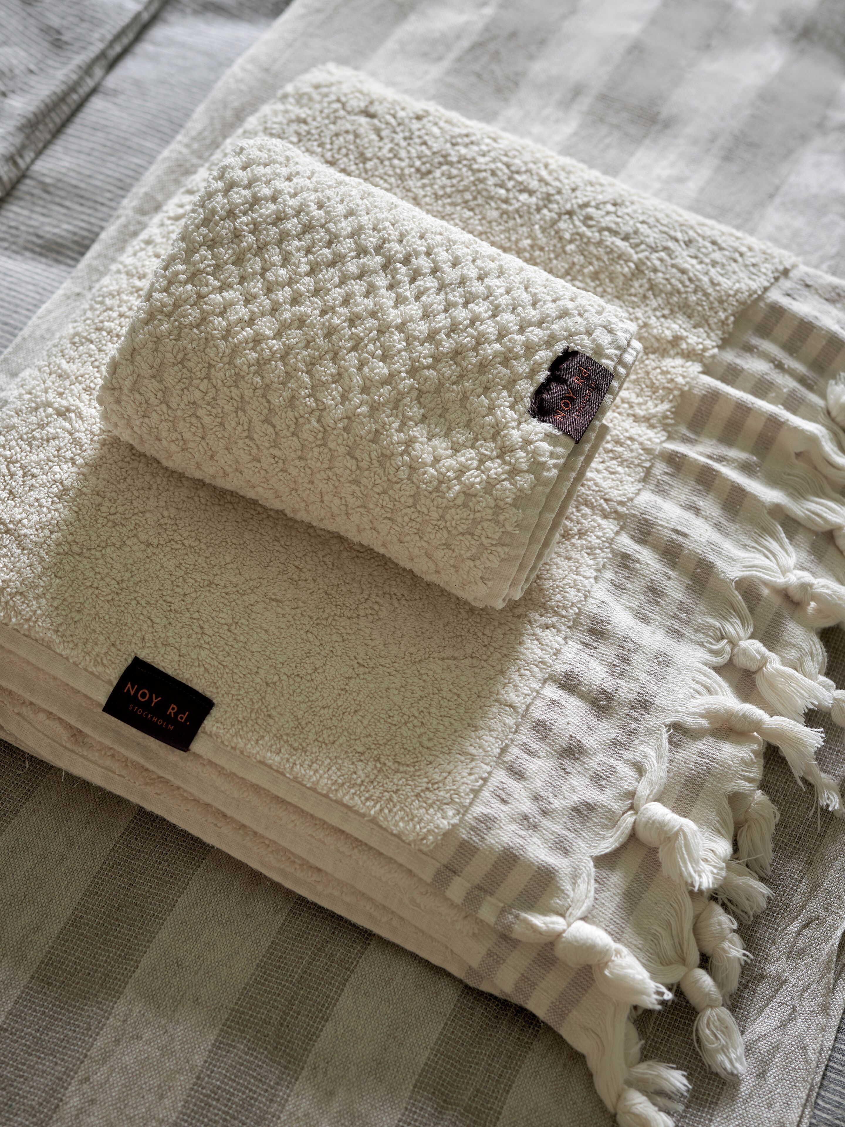 A stack of white textured blankets with tassels, one labeled 'Noy Rd. Stockholm'.