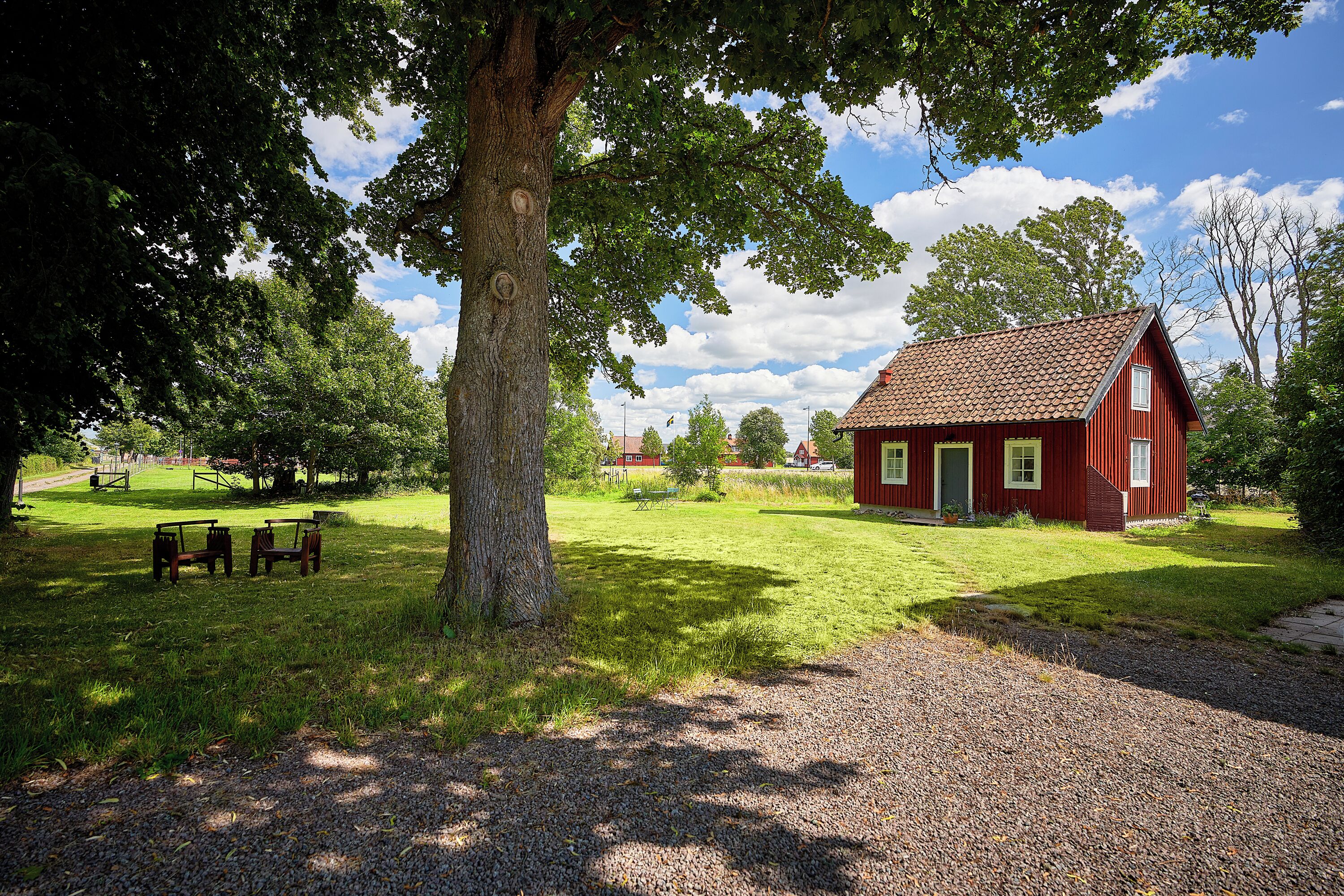 A red wooden house with a gravel path leading to it, surrounded by grass and trees.