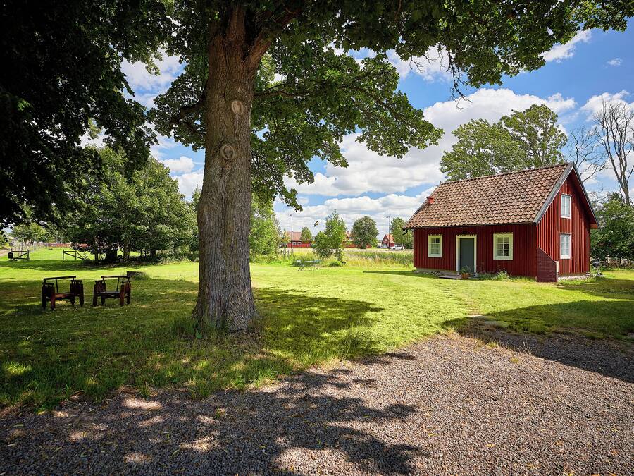 Ein rotes Holzhaus mit einem Kiesweg, umgeben von Gras und Bäumen.