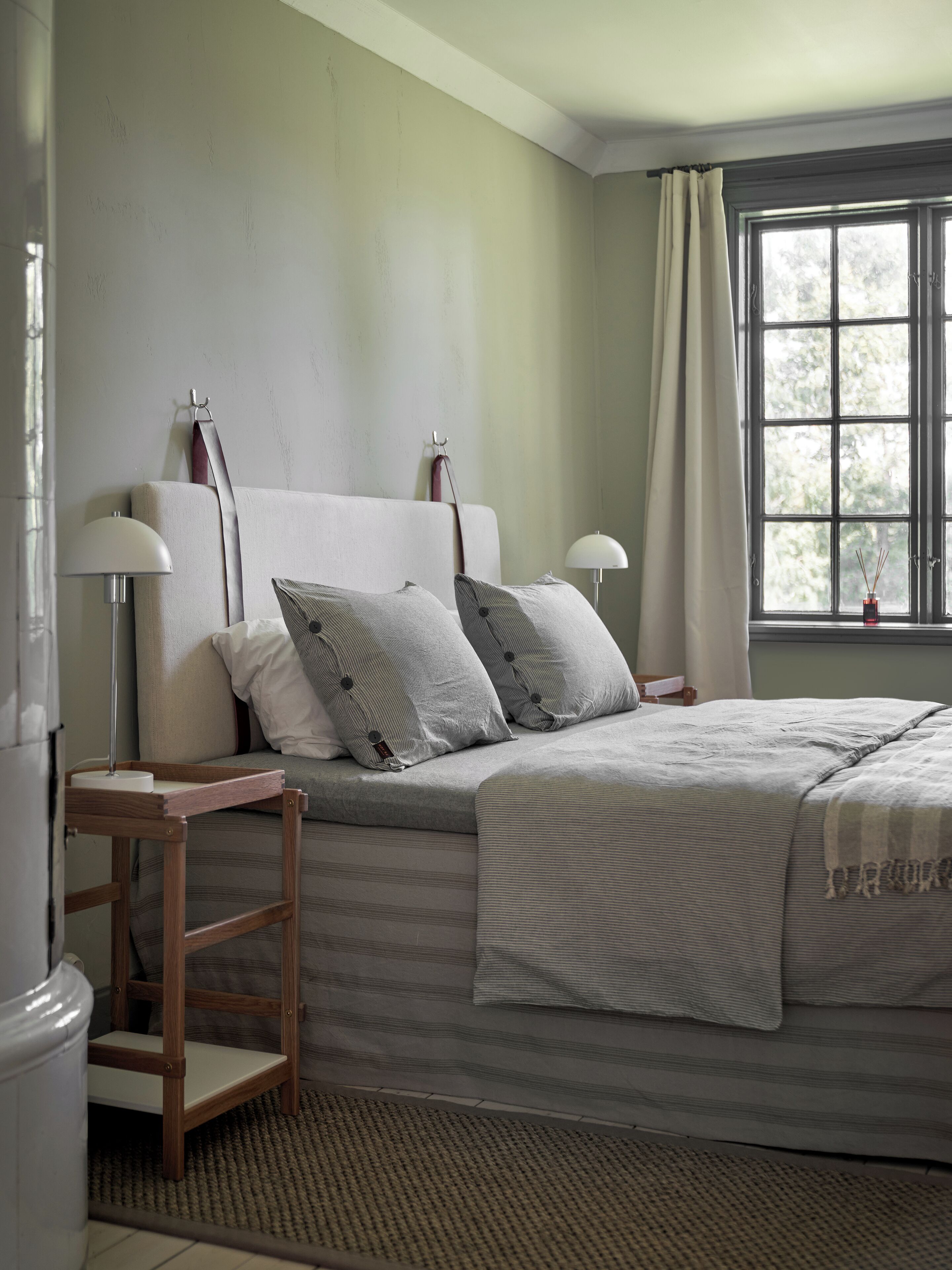 Une chambre à coucher avec un lit, des tables de chevet, des lampes, une fenêtre avec des rideaux et une vue sur les arbres.