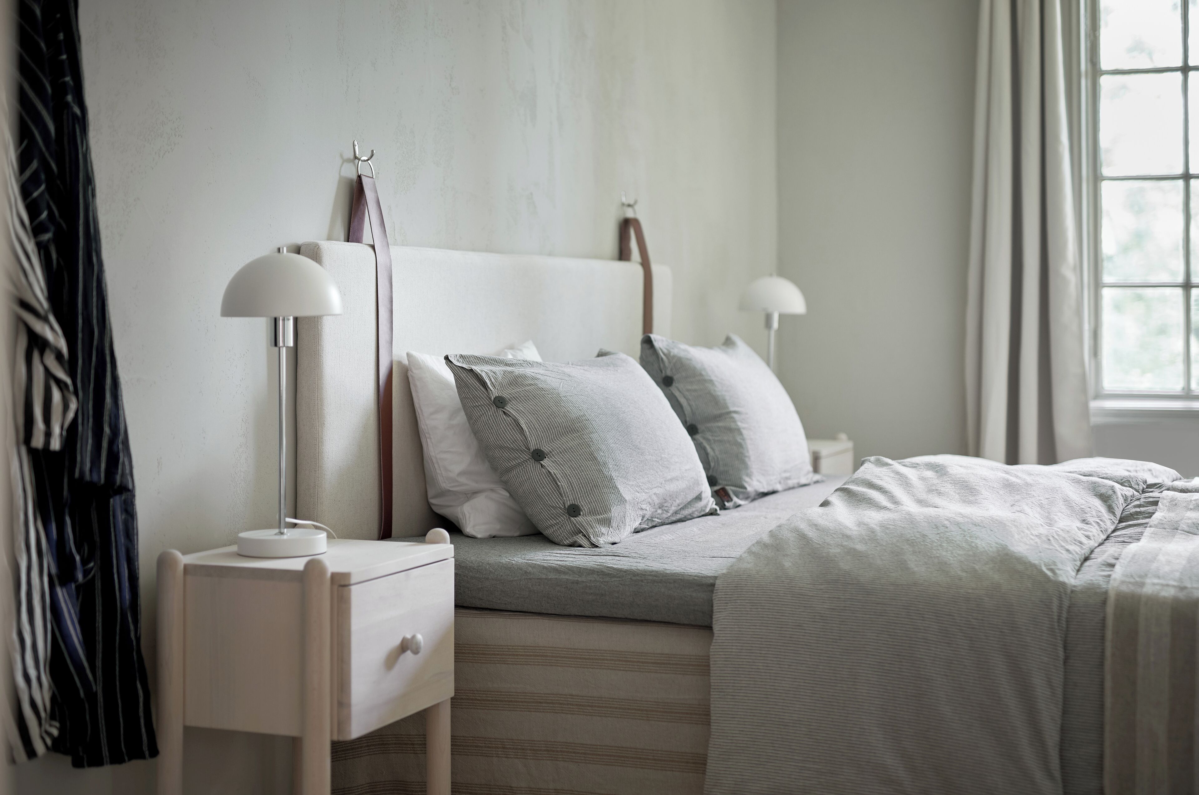 Un dormitorio con cama, lámparas de noche, mesita de noche y una ventana con cortinas.