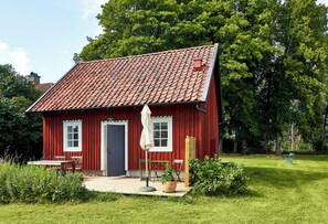 A red wooden house with a tiled roof, a door, and a small porch with a table and chairs.
