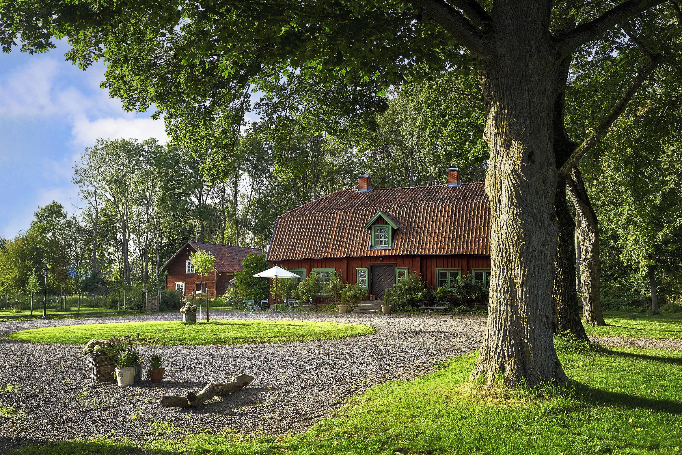 Ett hus med ett rött tak, omgivet av en grusuppfart, träd och en gräsyta.