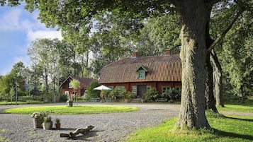 Ett hus med ett rött tak, omgivet av en grusuppfart, träd och en gräsyta.