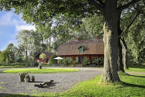 A house with a red roof, surrounded by a gravel driveway, trees, and a grassy area.