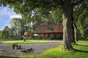 A house with a red roof, surrounded by a gravel driveway, trees, and a grassy area.