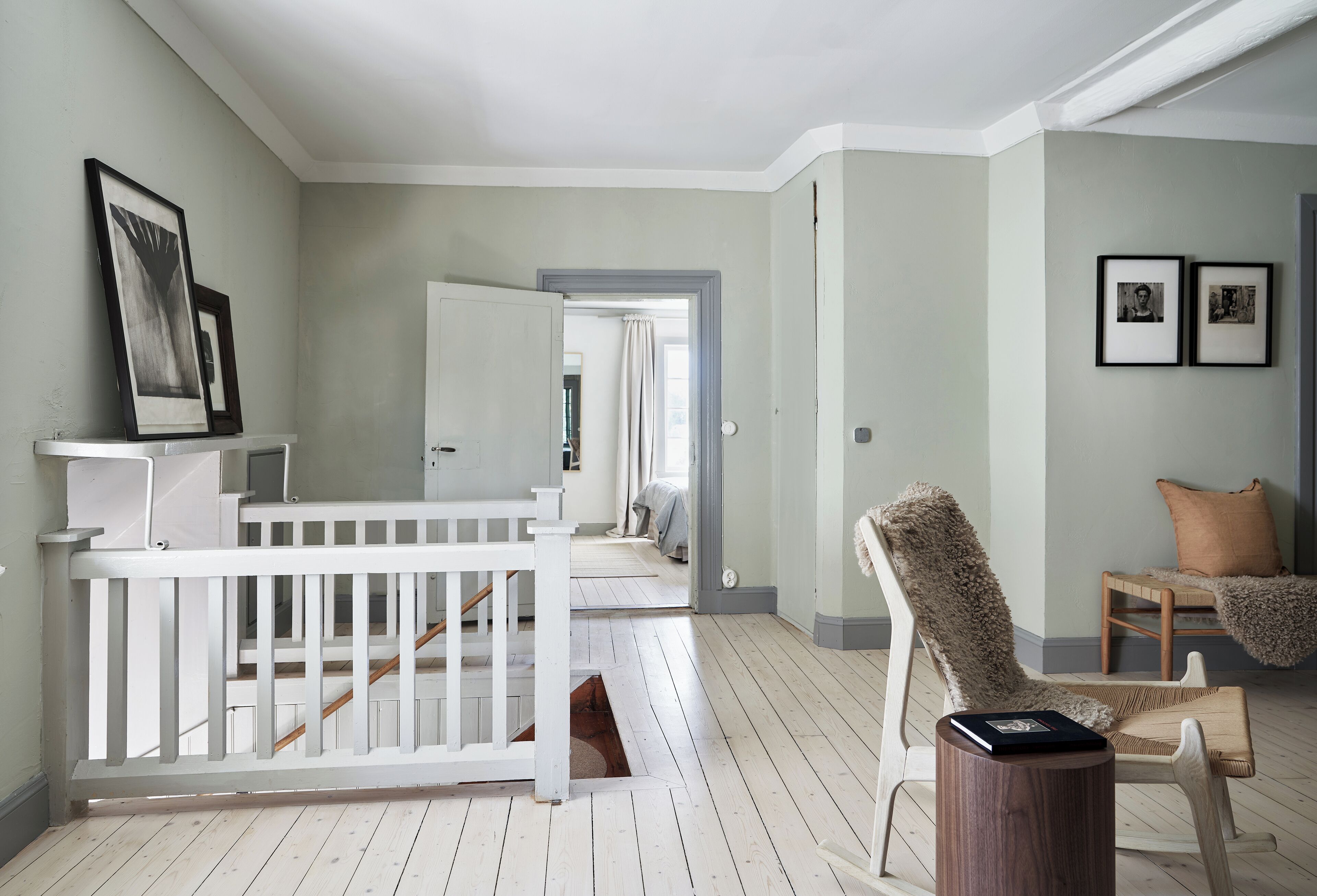 A spacious hallway with a white railing, a wooden floor, and a cozy seating area with a chair and a small table.