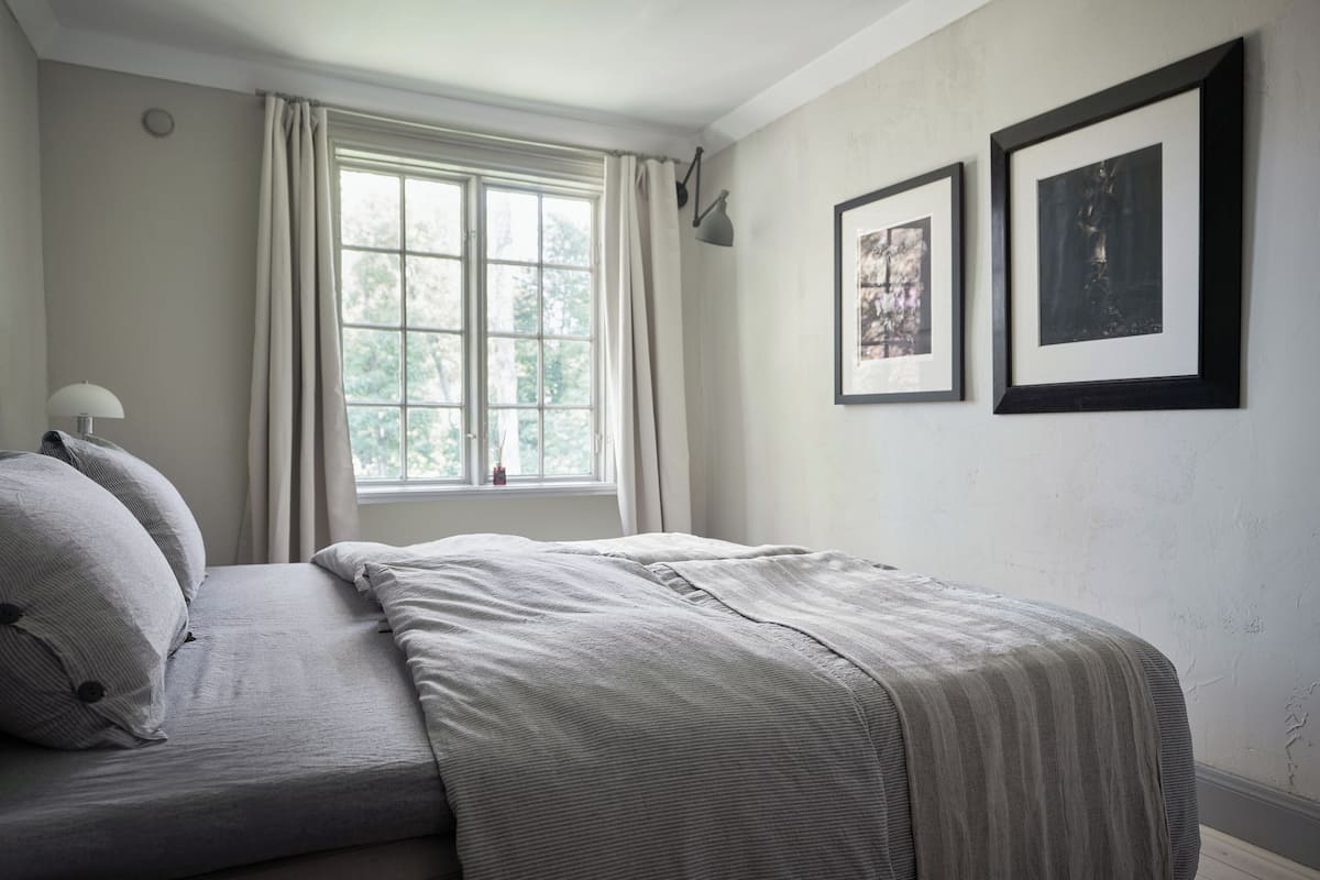 A bedroom with a bed, a window with curtains, and two framed pictures on the wall.