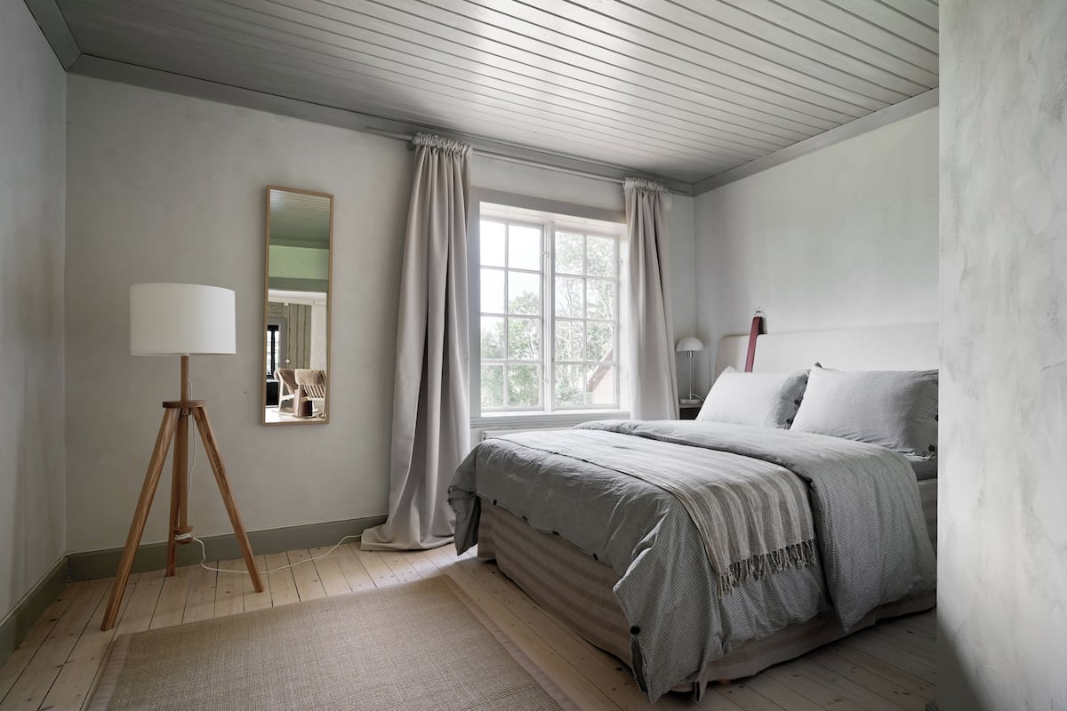 A bedroom with a bed, a lamp, a mirror, and a window with curtains.