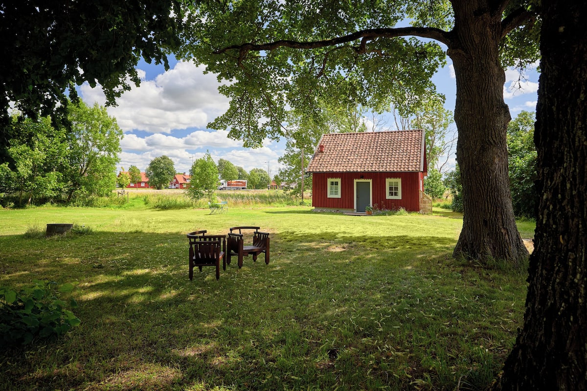 A red house with a tiled roof, surrounded by a grassy area and trees.