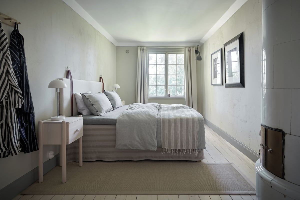 A bedroom with a bed, a nightstand, a lamp, a window with curtains, and a door.