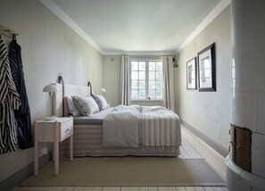 A bedroom with a bed, a nightstand, a lamp, a window with curtains, and a door.