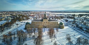 A large historic building with multiple domes and towers, surrounded by snow-covered trees and a river.