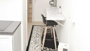 Un couloir étroit avec un petit coin cuisine comprenant une table, une chaise et une machine à café.