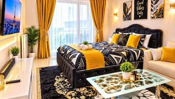 A modern hotel room with a large bed, a sofa, a glass coffee table, and a TV on the wall.