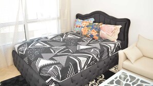 Une chambre à coucher avec une couvre-lit à motifs noir et blanc, une tête de lit capitonnée et deux coussins aux motifs colorés.