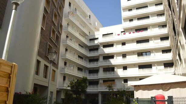 Un immeuble résidentiel à plusieurs étages, doté de balcons, d’une cour intérieure et d’une entrée sécurisée par un portail.
