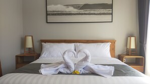 Ein ordentlich bezogenes Bett mit einer Handtuchskulptur in der Mitte, einem gerahmten Bild an der Wand und Nachttischlampen.