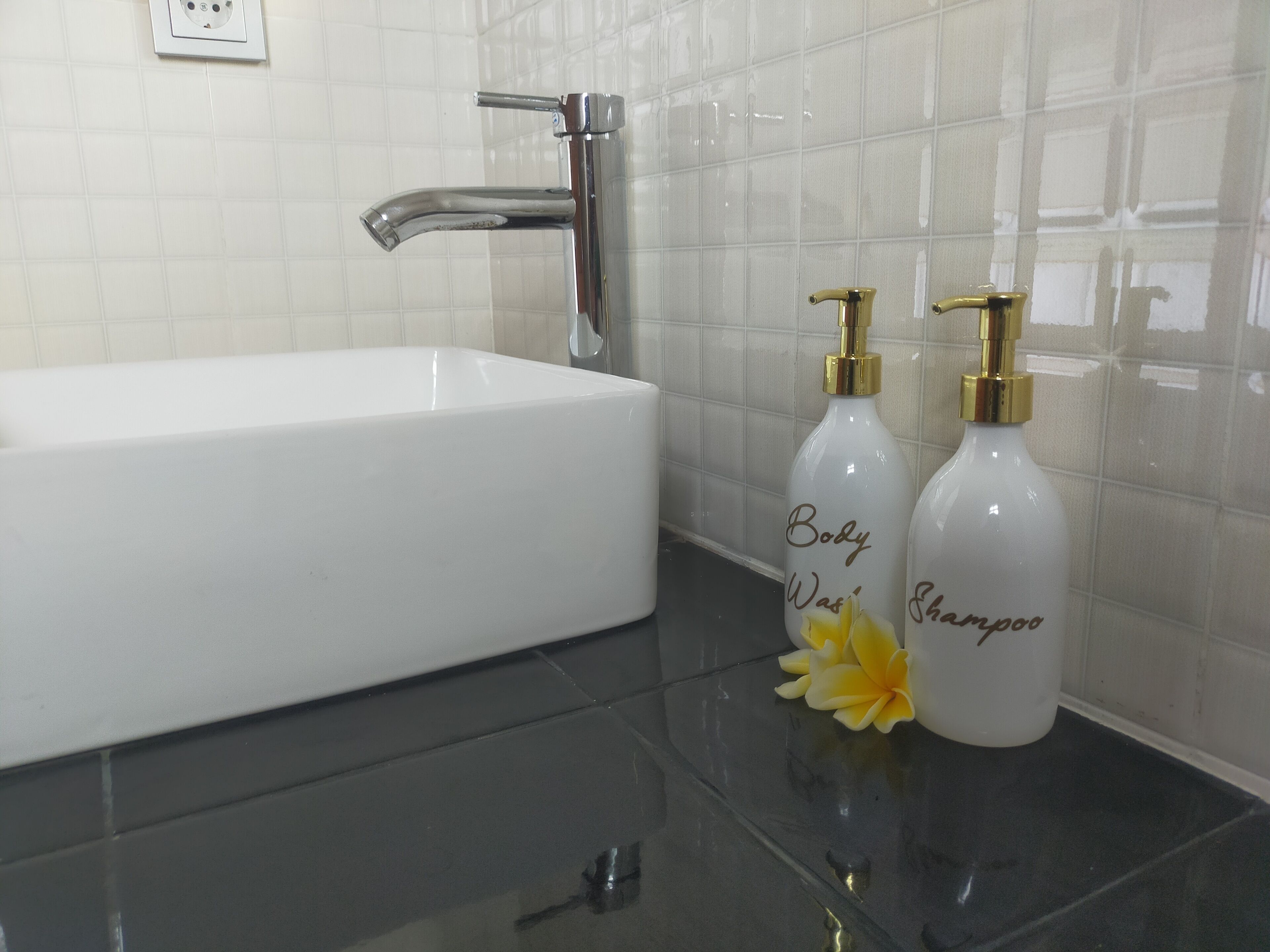 A bathroom with a white sink, a chrome faucet, and two white bottles labeled "Body Wash" and "Shampoo" with gold pumps.