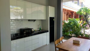 Eine moderne Küche mit weißen Schränken, einer schwarzen Arbeitsplatte und einem Kühlschrank. Ein Esstisch mit Stühlen und einer kleinen Pflanze steht daneben.