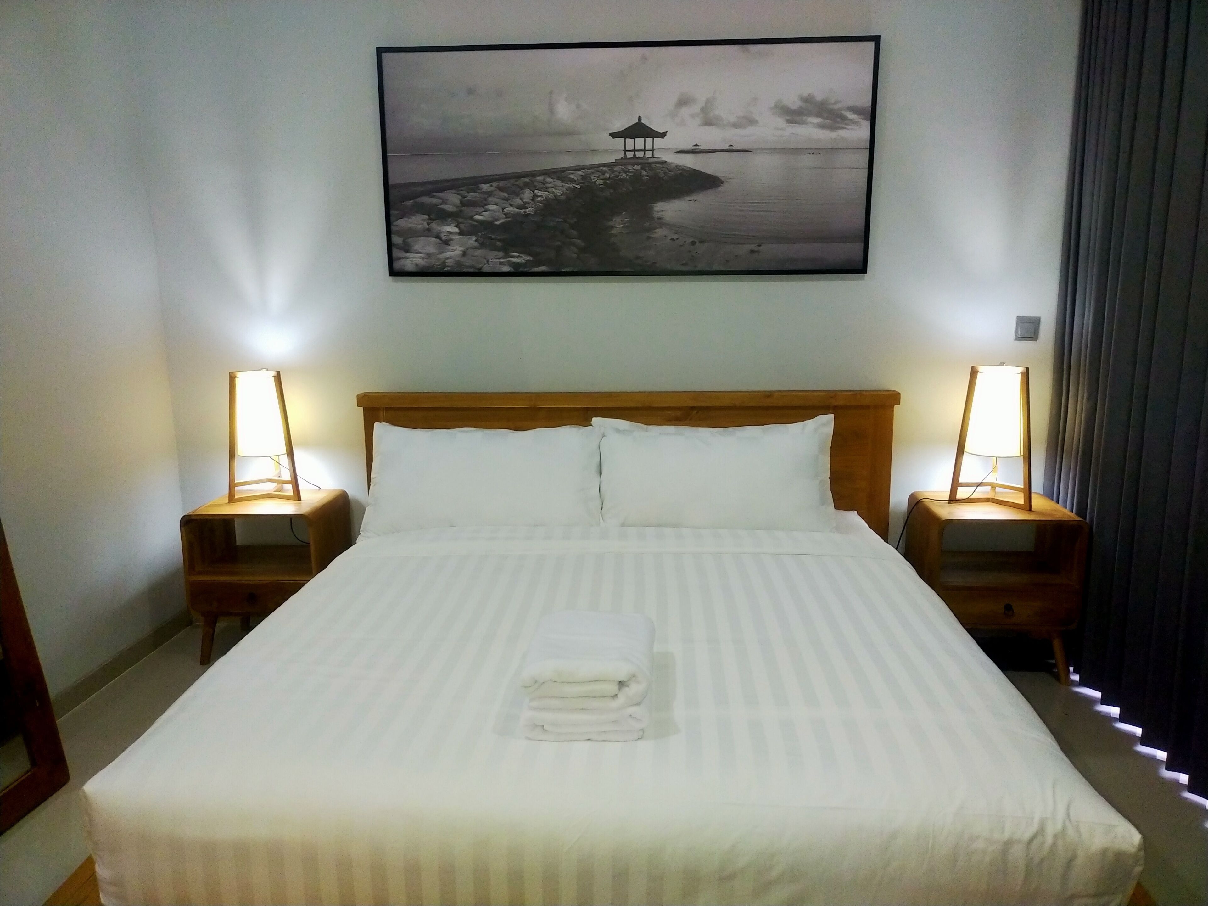 A hotel room with a large bed, two bedside tables with lamps, a framed picture on the wall, and a neatly made bed with a folded towel.