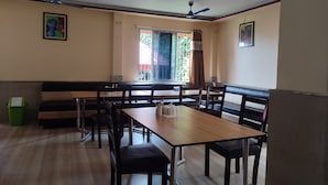 Un comedor con mesas y sillas de madera, un techo alto con iluminación empotrada y un ventanal con cortinas.