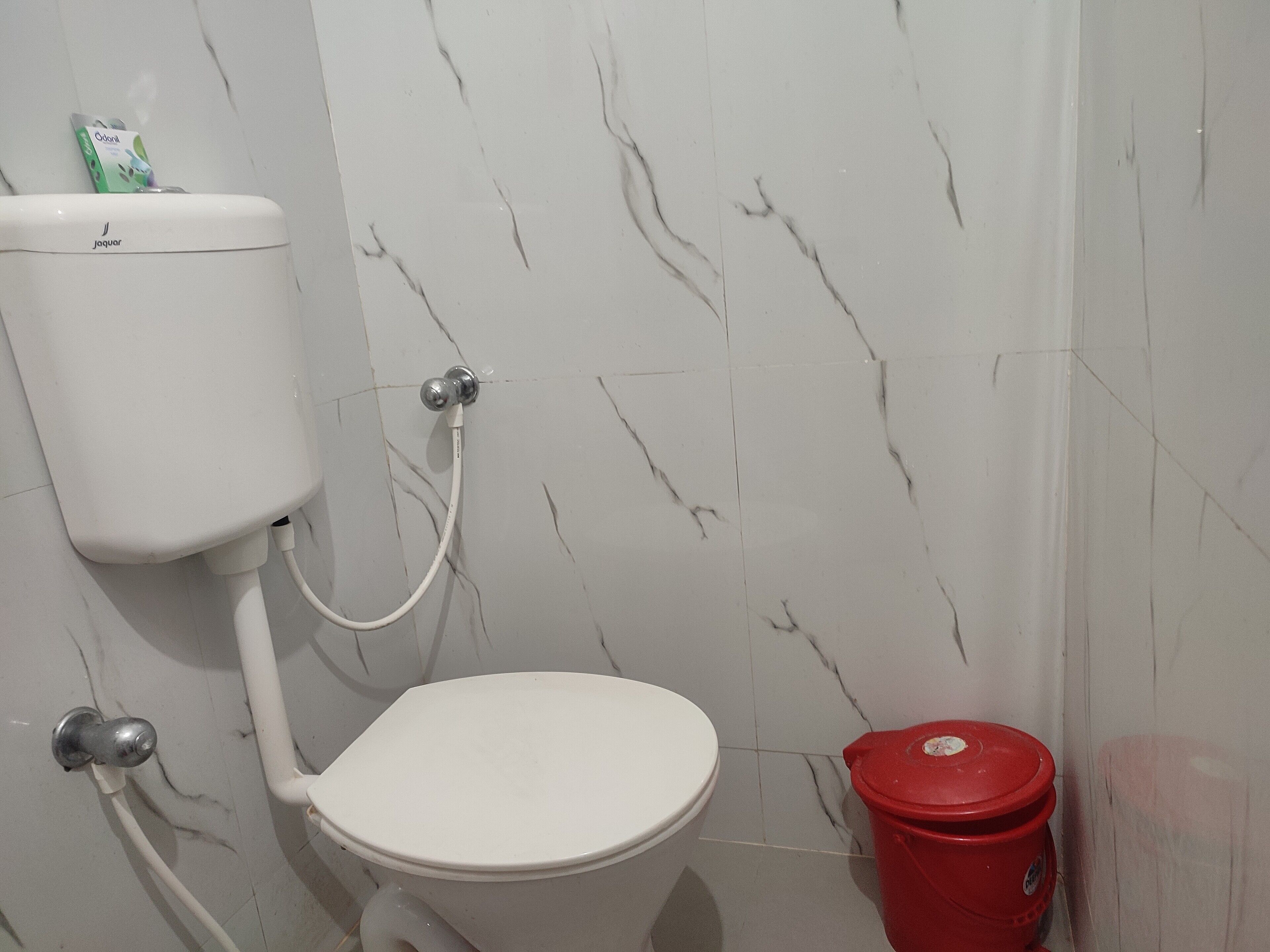 Un baño con inodoro, un sujetabebés blanco y un cubo de basura rojo.