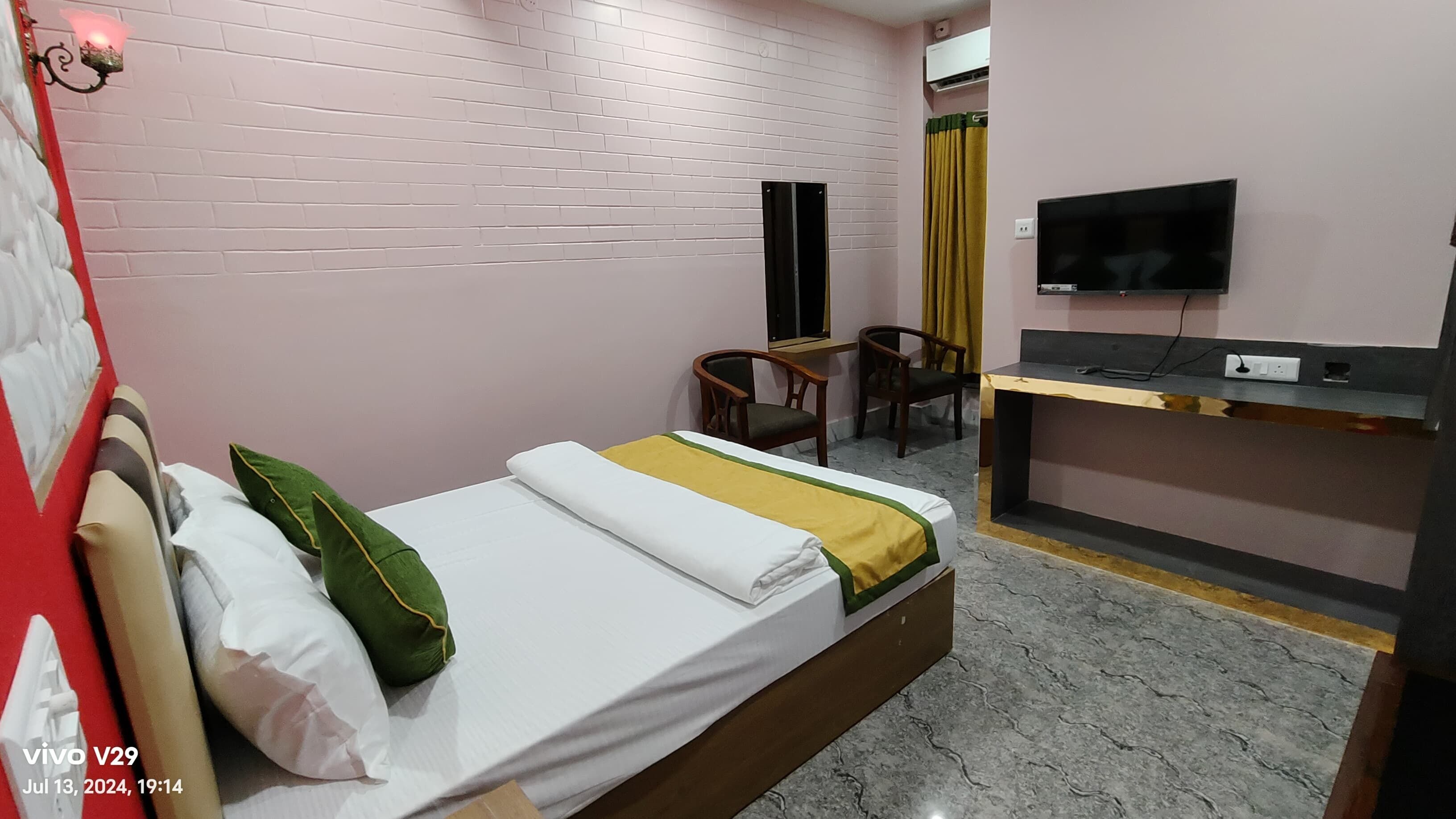 A hotel room with a bed, a desk, a chair, a TV, and a wall-mounted air conditioner.