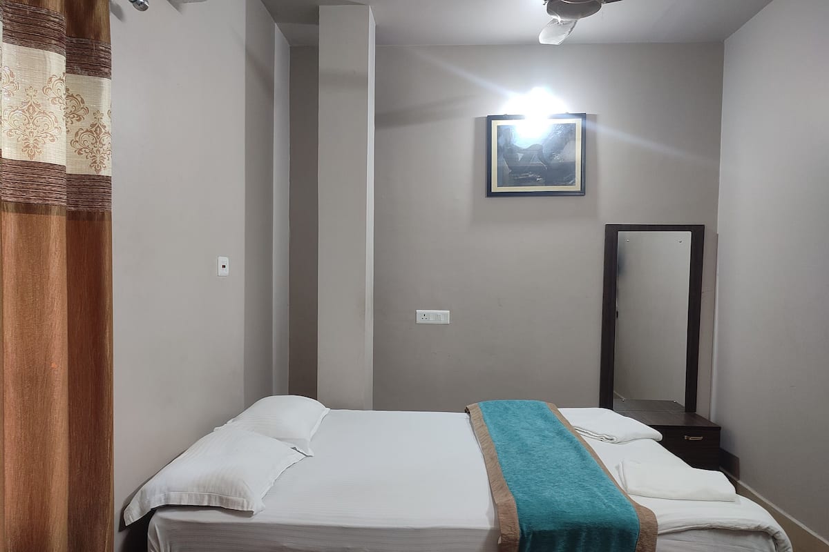 A bedroom with a bed, a bedside table, a mirror, and a wall-mounted light fixture.