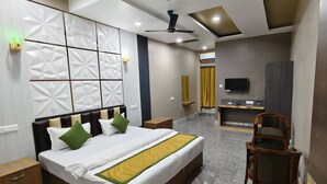 Habitación de hotel con cama, mesitas de noche, escritorio, silla, televisor y ventilador de techo.