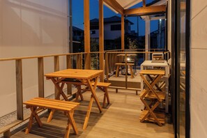 A wooden deck with tables and benches, a small table with a chair, and a glass door leading to a balcony.
