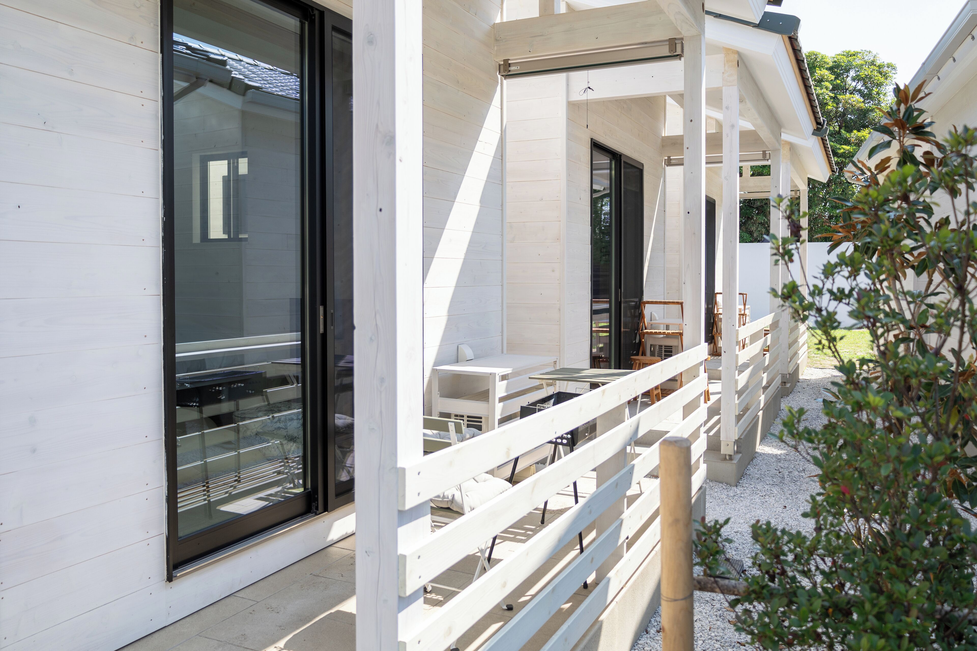 A modern building with large windows, a covered outdoor seating area, and a wooden fence.