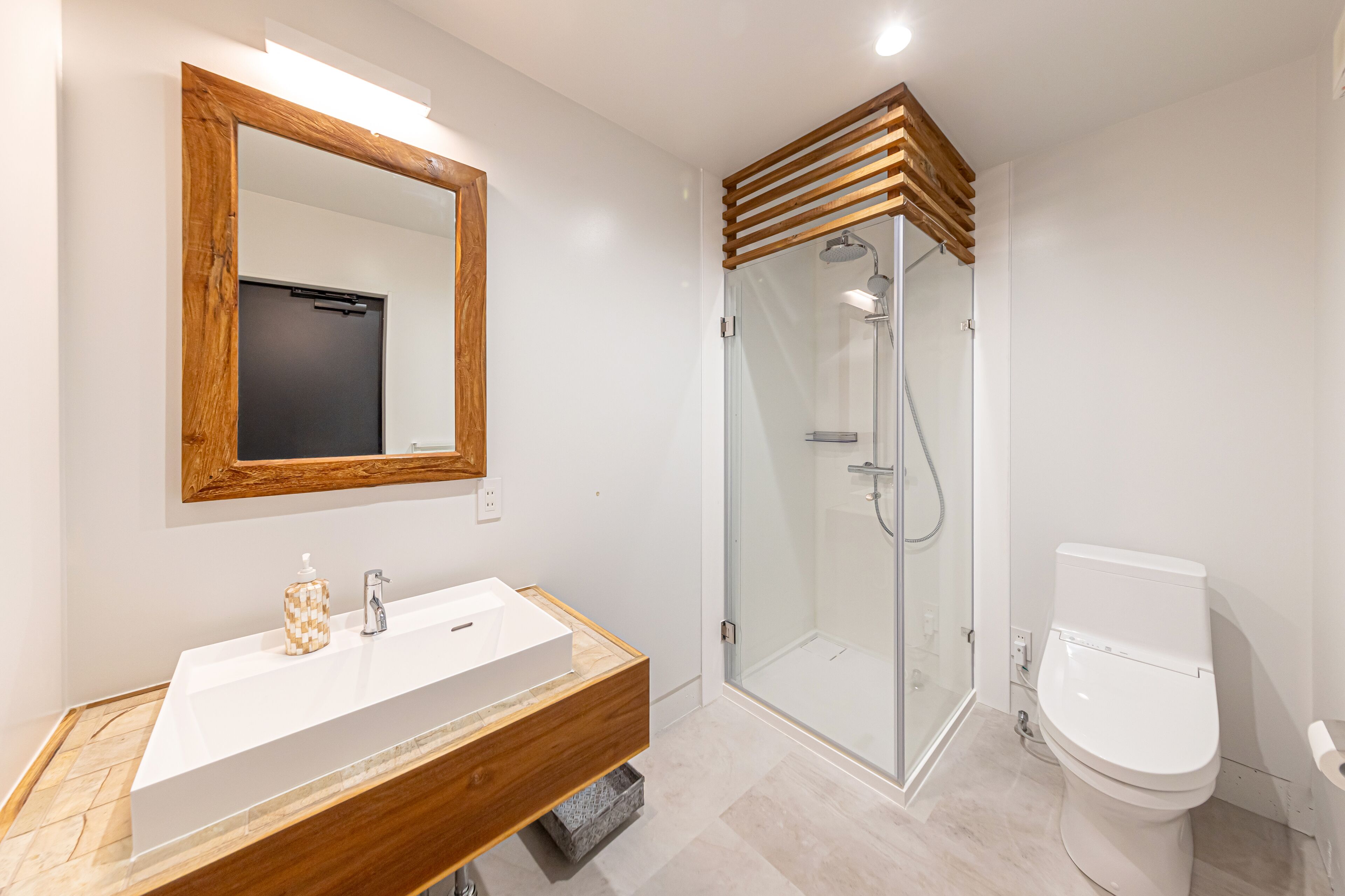 Une salle de bain moderne avec un meuble-lavabo en bois, une cabine de douche en verre et des toilettes blanches.