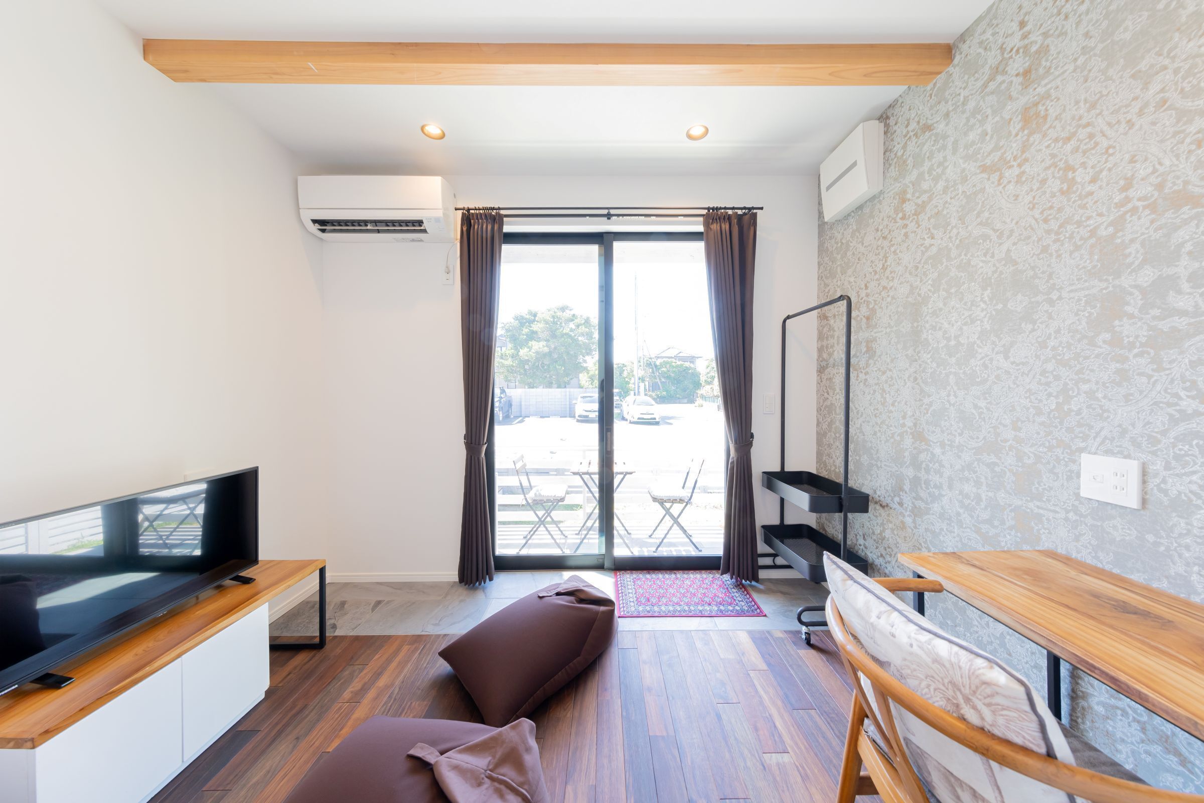A modern hotel room with a flat-screen TV, a sofa, a small table, a mirror, and a view of the outside through a glass door.