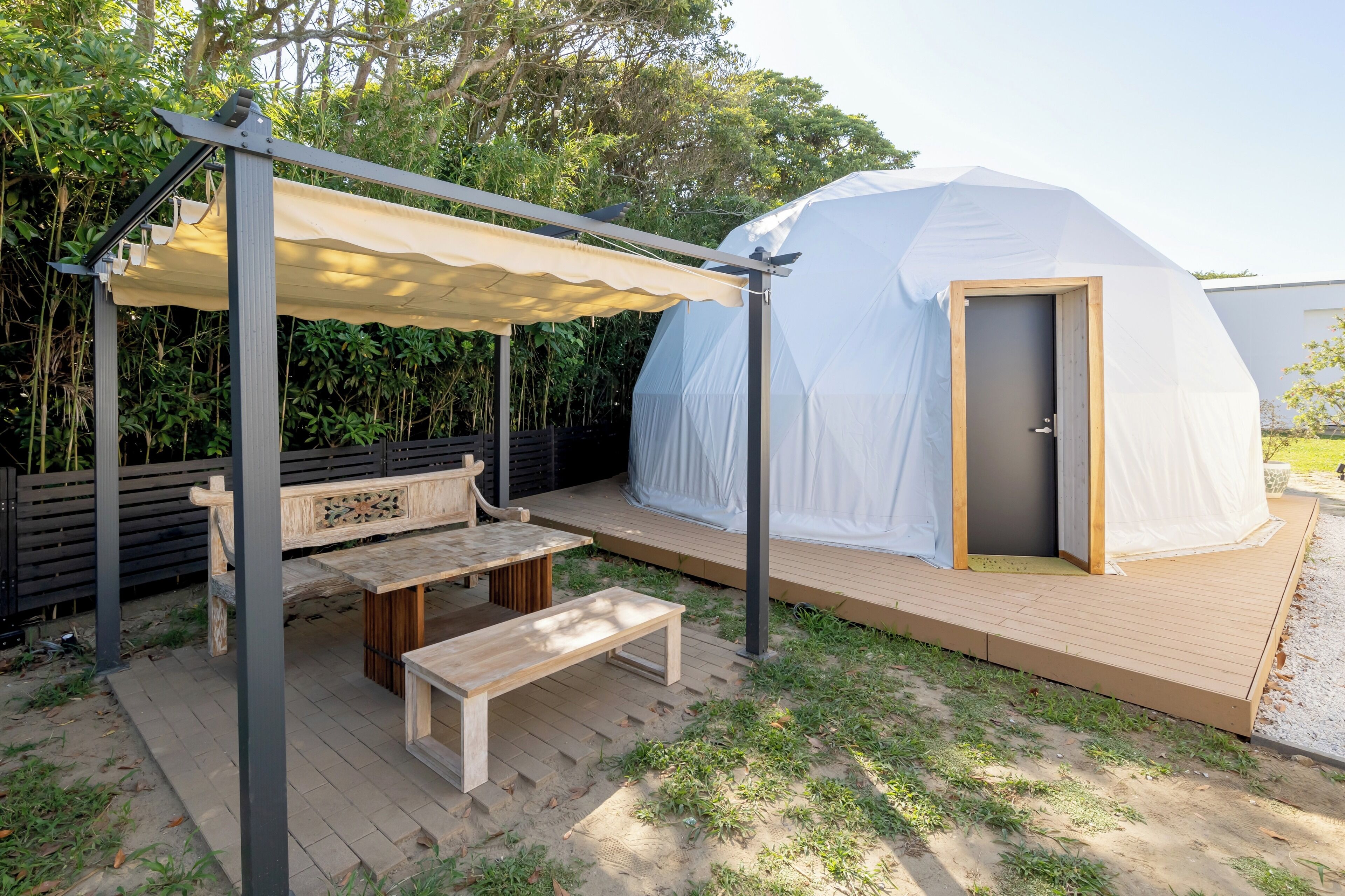 A covered outdoor seating area with a bench and table, a white tent-like structure, and a wooden deck.